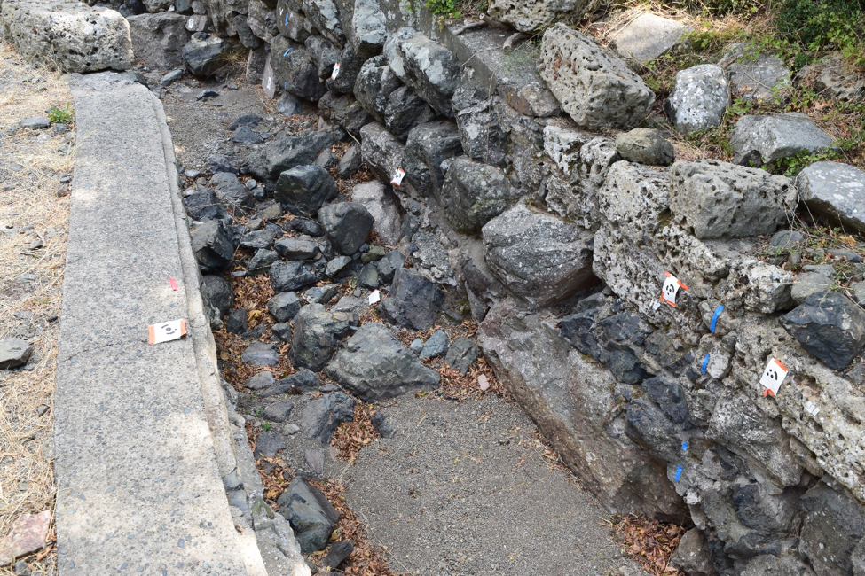 Modern concrete retaining wall beside ancient basalt masonry in the Central Ravine.